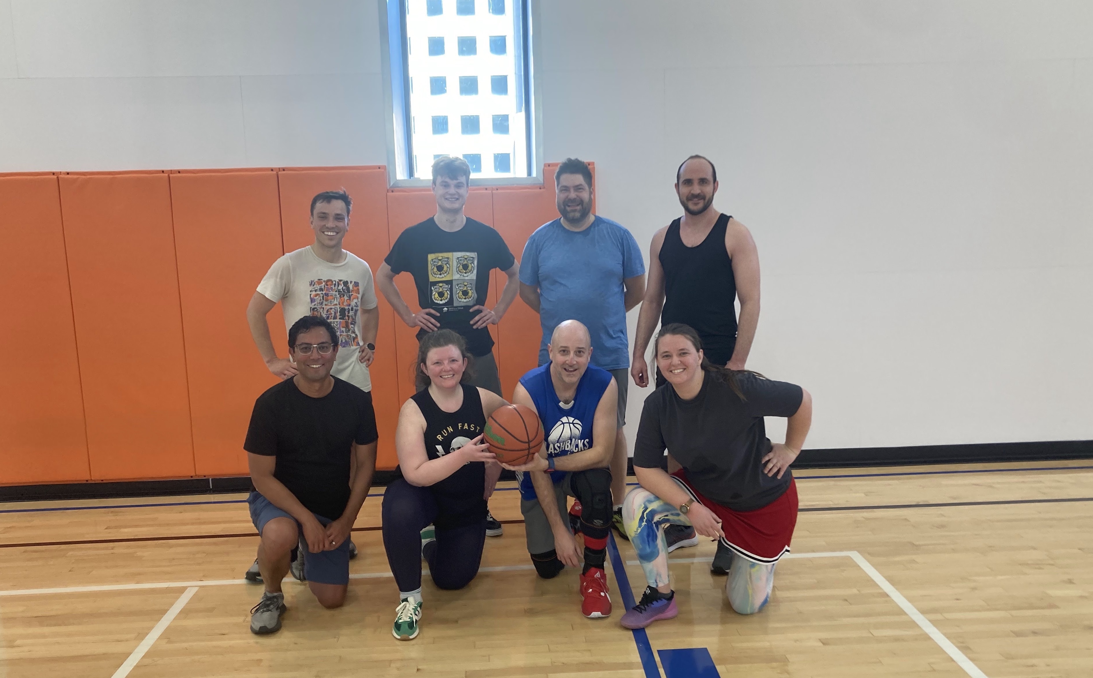 A group of 8 journalists attending NICAR 2025 lined up for a team photo at the halfcourt line of an indoor basketball court in Minneapolis.