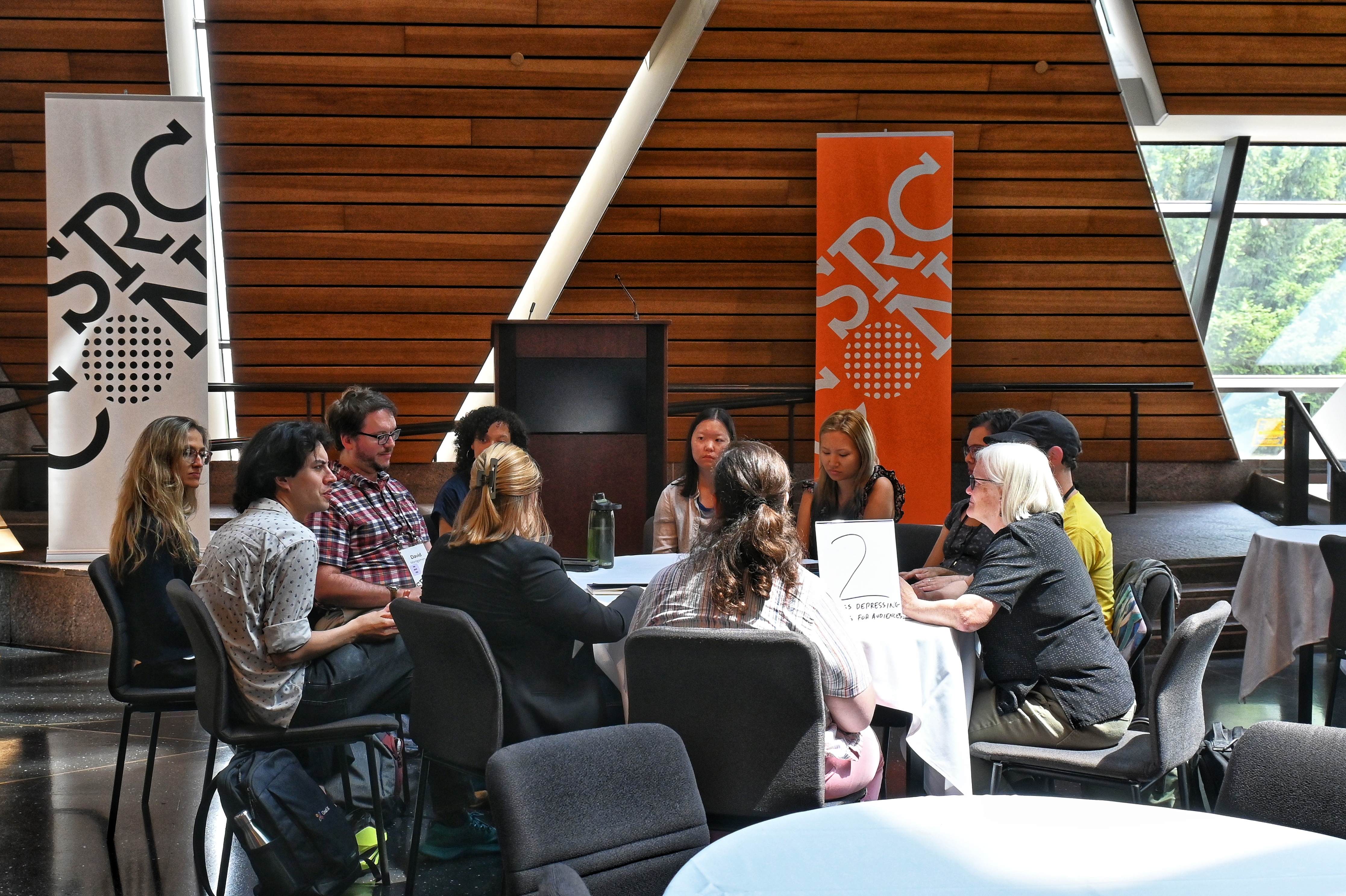 An overhead view of Memorial Hall at Source-con 2025 in Minneapolis with conference attendees sitting around tables under the skylights of the main seating area.